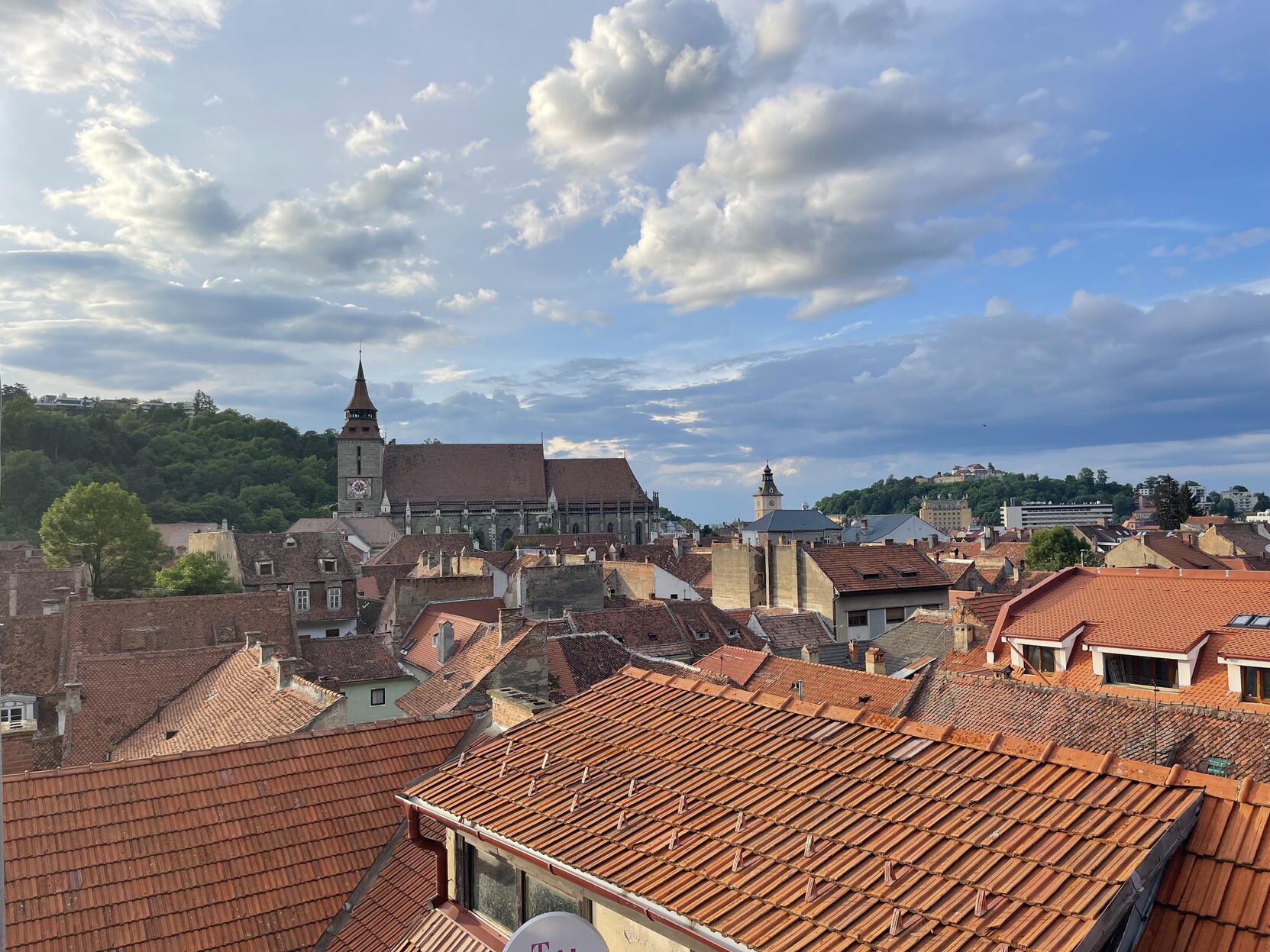 orange tile rooftops of Brașov, plus a view if Biserica Neagra (“the Black Church”) under blue, partly cloudy sky.